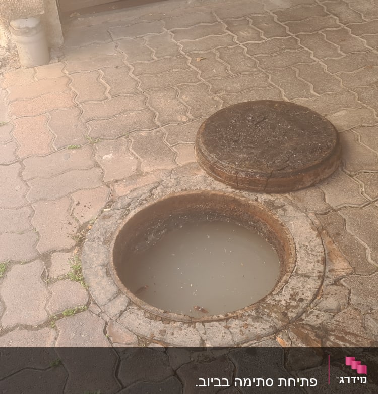 פתח ביוב פתוח עם מכסה מונח בצד